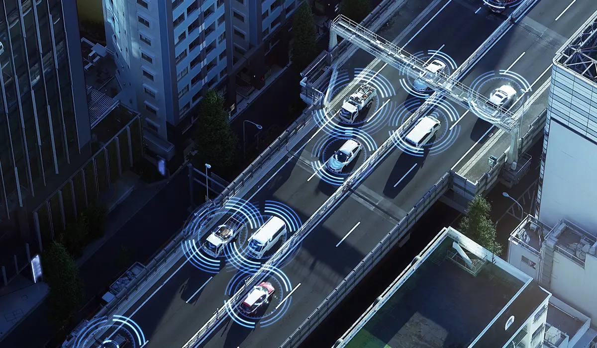 Several vehicles move along a city highway, surrounded by circular signal patterns that represent the sensors and communication of autonomous systems.