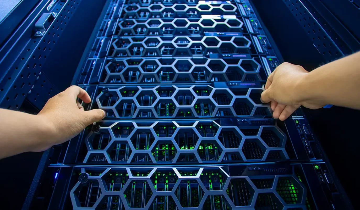 Zwei Hände bedienen ein Serverrack in einem Rechenzentrum, dessen wabenförmige Frontgitter den Blick auf grün leuchtende Hardwarekomponenten freigibt.