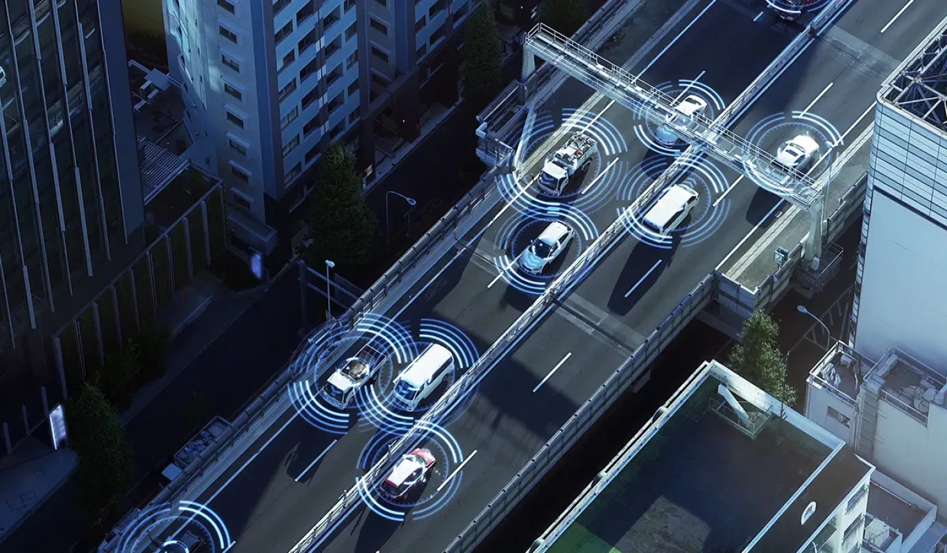 Mehrere Fahrzeuge bewegen sich auf einer Stadtautobahn, umgeben von kreisförmigen Signalmustern, die die Sensorik und Kommunikation autonomer Systeme darstellen.